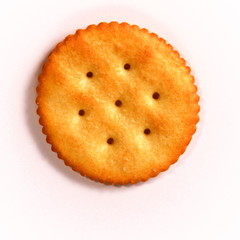 Top view of single round buttery cracker with holes and salt on white background.