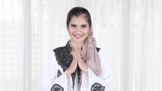 Attractive young Asian muslim woman smiling at the camera and showing a greeting gesture at home. Shot in 4k resolution