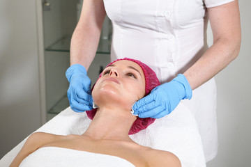 Obraz premium A cosmetologist puts a remedy on the face for the patient to nourish, moisturize and rejuvenate the skin. Cosmetic procedure in the clinic. Close-up of the patient's face.
