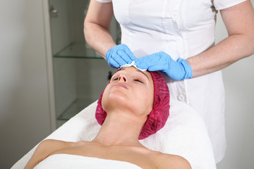 A cosmetologist puts a remedy on the face for the patient to nourish, moisturize and rejuvenate the skin. Cosmetic procedure in the clinic. Close-up of the patient's face.