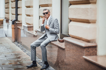 Stylish old businessman siting an the terrace and looking forward to with his favourite cigarette