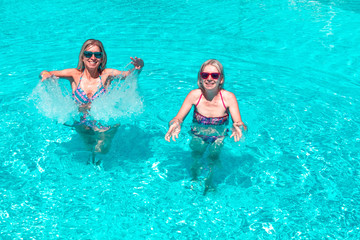 Two young blonde woman with colourful bikini enjoying. Happy gorgeous females with stylish sunglasses and bikini relaxing in the swimming pool at resort spa