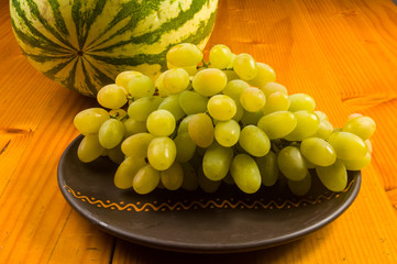 large brush of green grapes and watermelon in a dark ceramic plate on a wooden background