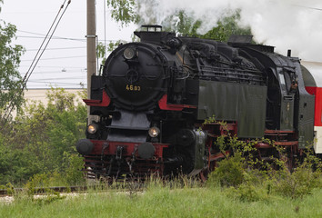Fototapeta na wymiar Historic steam locomotive with passenger wagons speeding on railroad tracks curve and blowing heavy white smoke near Sofia