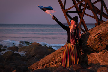 Girl at the beach with Estonian national clothes and flag.