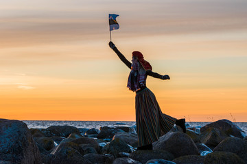 Girl at the beach with Estonian national clothes and flag.