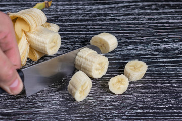 A man cuts a banana knife into slices on an old black wooden table