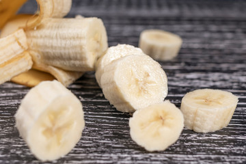 Sliced and peeled not completely banana and its pieces lie on a dark wooden background