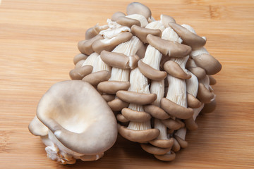 Fresh oyster mushroom clusters laid out on a natural bamboo cutting board.