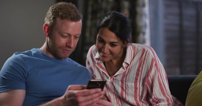 4K Couple relaxing at home & looking at smartphone & woman reacting with surprise. Slow motion.