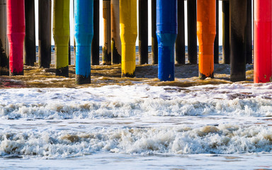 Foamy waves breaking through the rainbow colored multicolor pier footings in the North sea on...