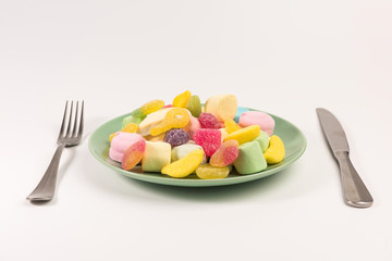Fork, knife and plate with marshmallow and gummy candies isolated on white background.