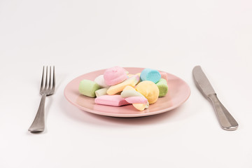 Fork, knife and pink plate with marshmallow isolated on white background.