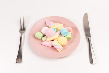 Fork, knife and pink plate with marshmallow isolated on white background.