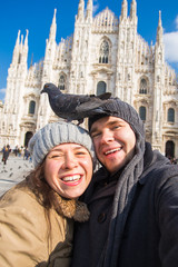 Couple taking self portrait with pigeon in Duomo square in Milan. Winter traveling, Italy and relationship concept