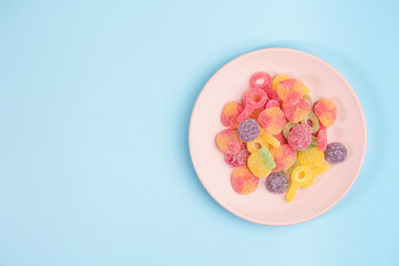 Pink plate with gummy candies on blue background. Top view.