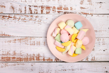 Pink plate with marshmallow on white wooden background. Top view.