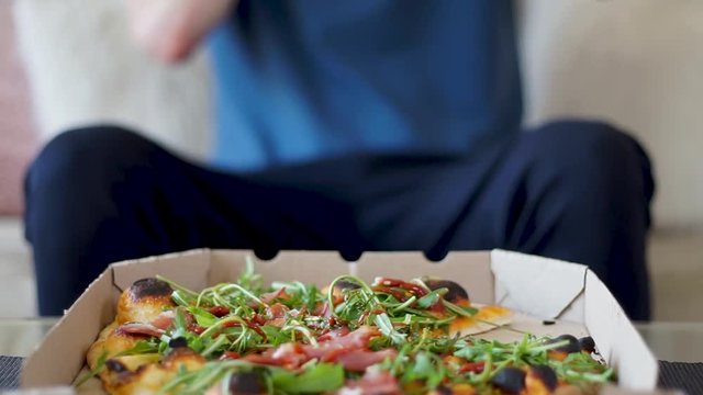 Young caucasian man taking a pizza slice with both hands from a box at his home