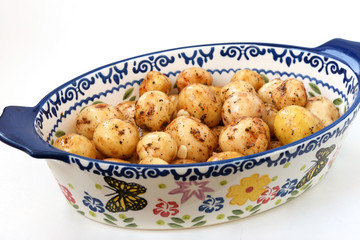 Young peeled potatoes in spices prepared for roasting in a ceramic form on a white background