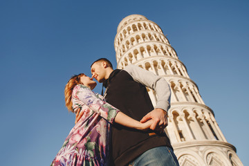 Fototapeta premium Loving couple takes selfie photo on stick and camera against background of leaning Tower Pisa, Italy. Travel concept