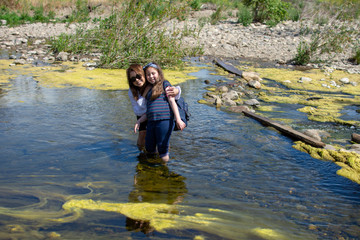 Woman and daughter standing and laughing tother while playing in a stream or river