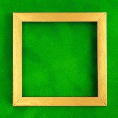 Square golden wooden frame on green velvet background.