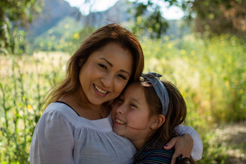 Latina Woman and daughter smiling together in front of a bright field at a park