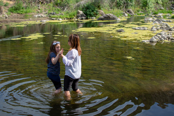 Woman and daughter standing and laughing together while playing in a stream or river