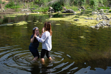 Woman and daughter standing and laughing together while playing in a stream or river