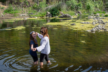 Woman and daughter standing and laughing together while playing in a stream or river