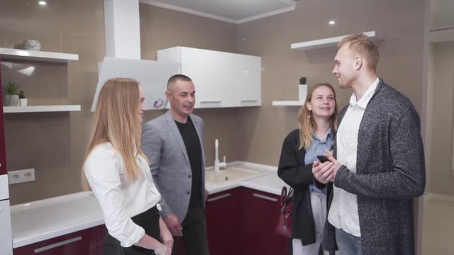Married Caucasian Couple Standing in Kitchen of New Apartment Property With Real Estate Brokers Talking and Recieving The Keys. Light Camera Movement