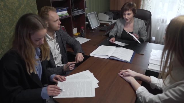 Couple New Buyers of Real Estate Property Sitting At Realtors Office and Looking at Contraxt Before Signing. Light Camera Movement