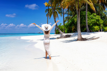 Attraktive Frau in weißem Sommer Kleid läuft an einem tropischen Strand mit Palmen und ist...
