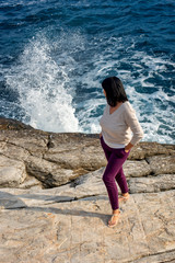 a young girl looks at the waves that break through the shore