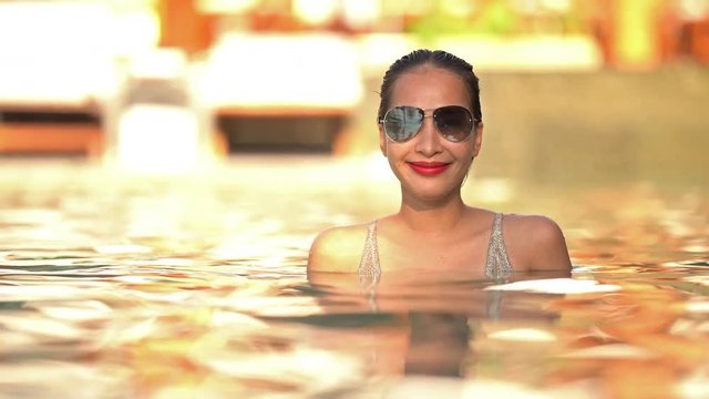 Static shot of a sexy smiling lady swimming in a pool wearing sunglasses