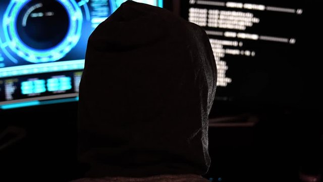 Close-up shot of cyber criminal hacker in a dark office with hi-tech screens
