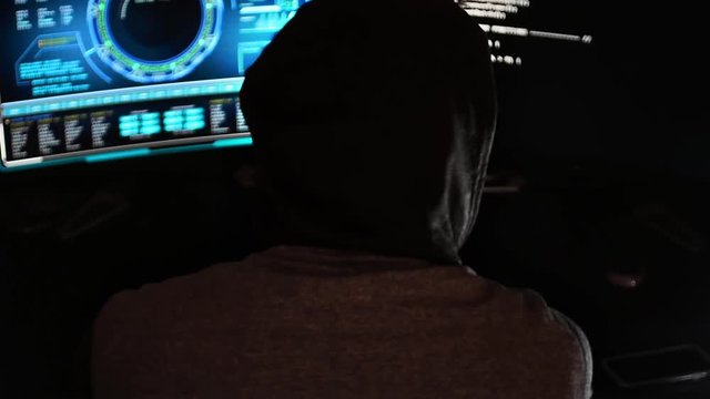 Wide shot of cyber criminal hacker in a dark office with hi-tech screens