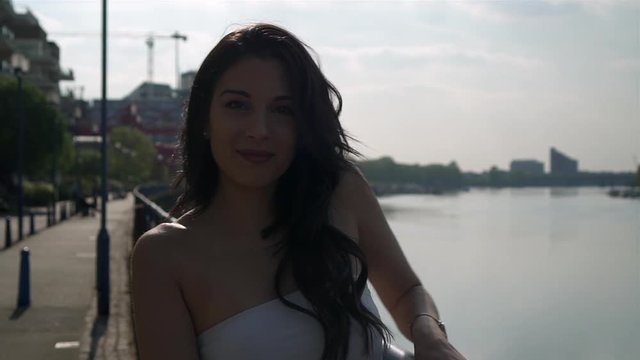 Beautiful latina woman on holiday turning and smiling at the camera right next to the river Thames in London.