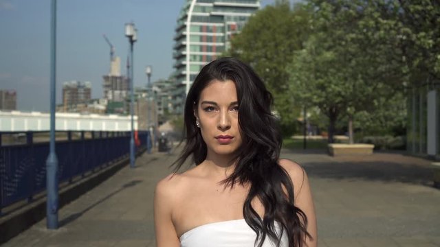 Attractive and playful hispanic latina woman walking towards the camera, on the riverbank of the Thames in London, UK
