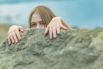 A young girl teenager on the shore hiding behind a stone
