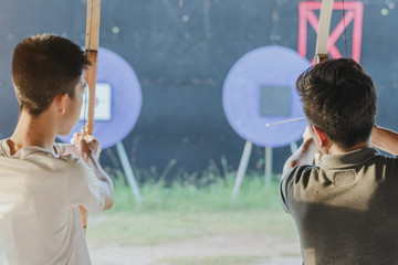 Obraz premium Tourists try to use a bow and arrow and shoot at a target in the amusement park.