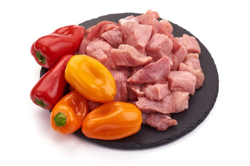 Raw pork pieces with vegetables on a slate shale plate, close-up, isolated on white background