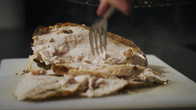 Slices of delicious looking and steaming hot roasted chicken breast on a white cutting board. Large knife carves another piece as the family meal is prepared.