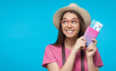 European Caucasian girl in hat and sunglasses isolated on background smiling with airplane tickets in hands