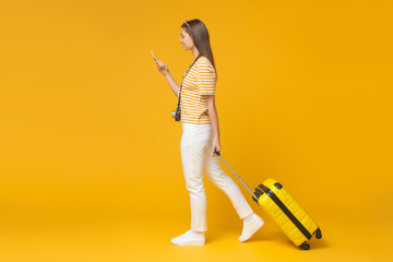 Full-size portrait of European girl isolated on yellow background walking with suitcase for...