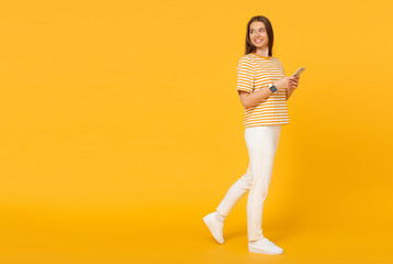 Fototapeta na wymiar Young caucasian woman walking and communicating via phone, isolated on yellow background with copy space on left