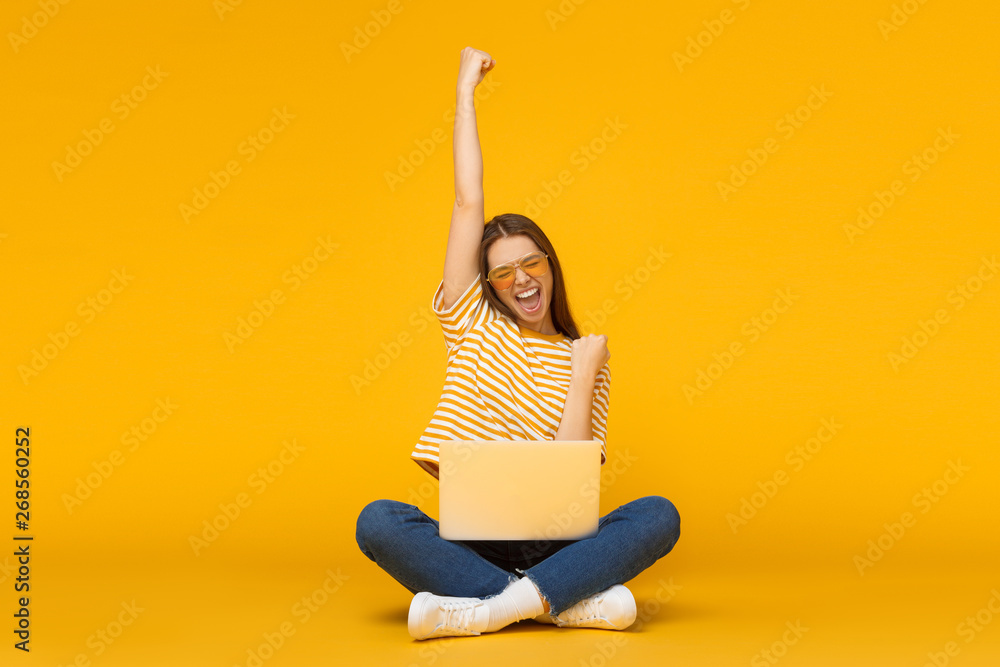 Wall mural she is a winner! excited young female with laptop isolated on yellow background - Wall murals