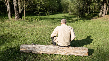 Fototapeta premium A man sits on a log in the forest. A man is resting in the forest.