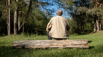 A man sits on a log in the forest. A man is resting in the forest.