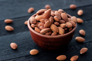 Almonds nuts in ceramic bowl on on the dark oak texture